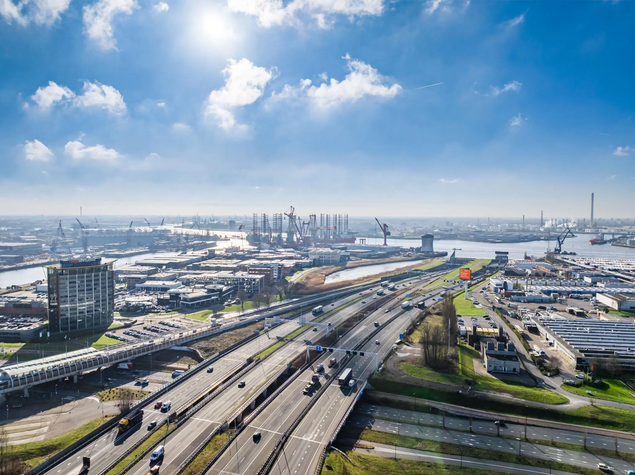 Luchtfoto van de Karel Doormanweg met snelwegen, industrieterrein en havengebied in de zon.